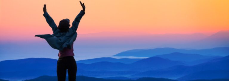 Woman raising her hands at a beautiful mountainous lookout at sunset