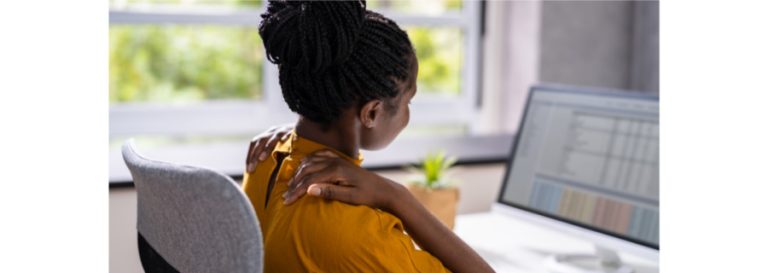 Office worker sitting at desk massaging sore shoulders