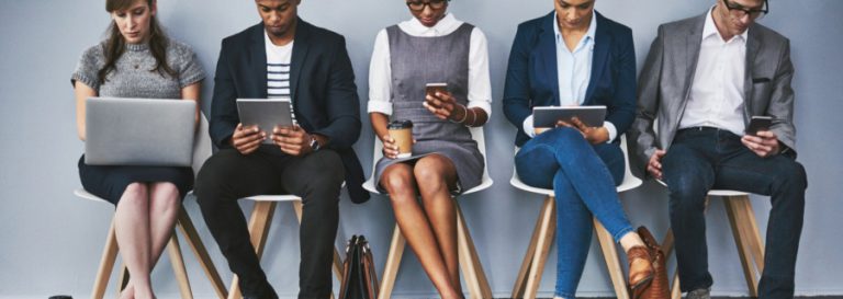 5 people sitting in chairs either on phones or laptops