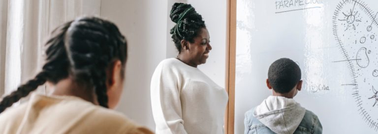 woman showing two children information on a whiteboard